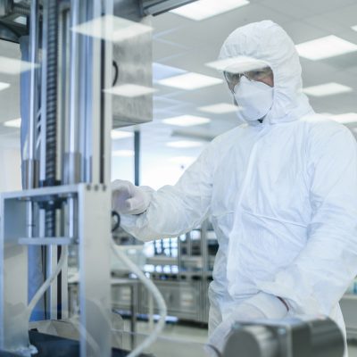In Manufacturing Facility Shot of Scientist in Sterile Protective Clothing Work on a Modern Industrial 3D Printing Machinery. Pharmaceutical, Biotechnological Manufacturing Process. Shot from Inside.